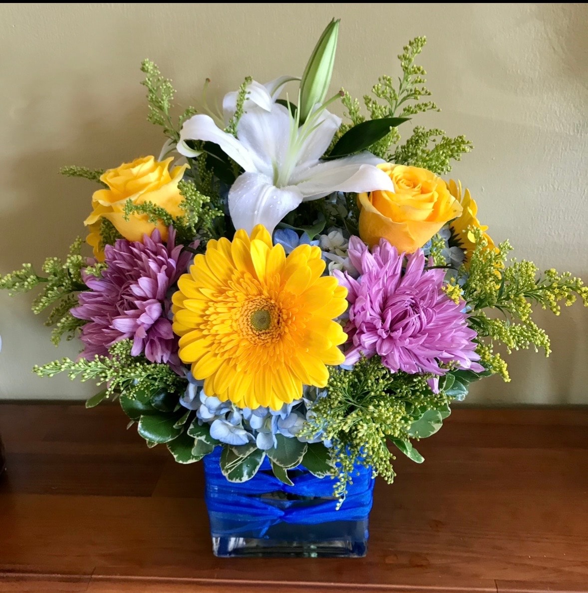 Everyday floral arrangement with yellow gerberas, purple dahlias, white lily and blue hydrangea in blue vase