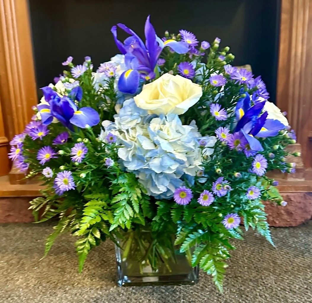 Everyday floral arrangement with purple irises, blue hydrangeas, white rose and purple asters in glass vase